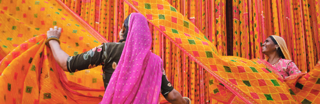Two women working with colorful sari textiles drying in the open air at a traditional textile factory in Rajasthan, India.