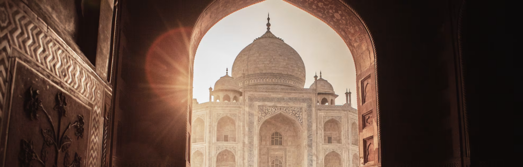 The Taj Mahal in Agra, India reflected in water at sunrise with soft golden light and clear skies.